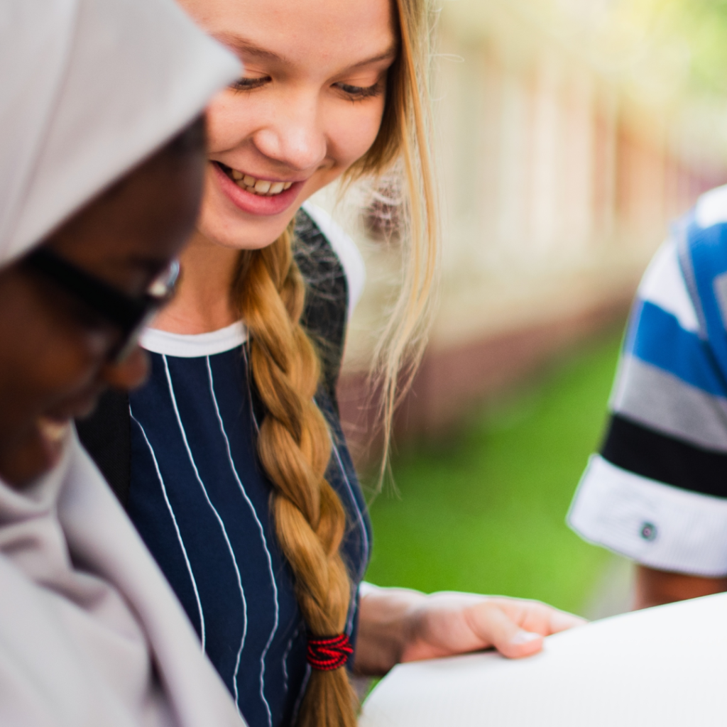 Diverse group of teenagers look at papers while smiling.