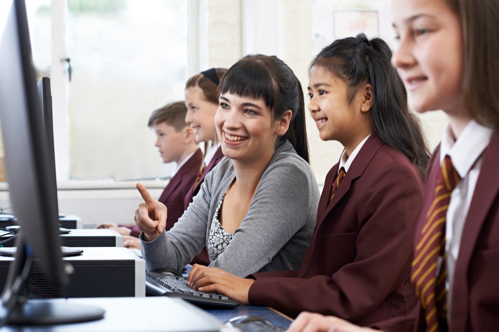 Pupils in maroon blazers in computer class with teacher.