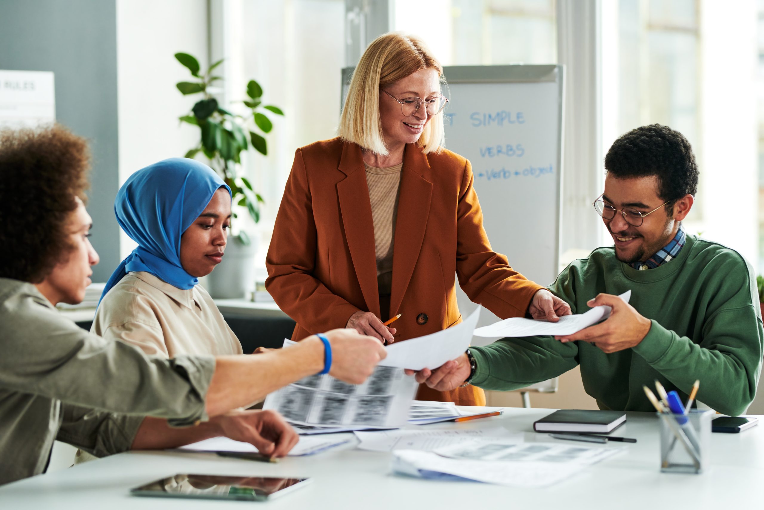 Happy mature teacher passing papers with grammar test or authentic materials
