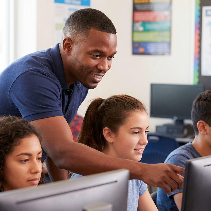teacher helping students on computer in lesson